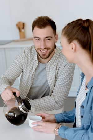 smiling husband pouring coffee for with wife on kitchen in morningの写真素材