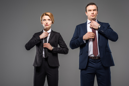 businesswoman and businessman fixing ties, isolated on grey, leader conceptの写真素材