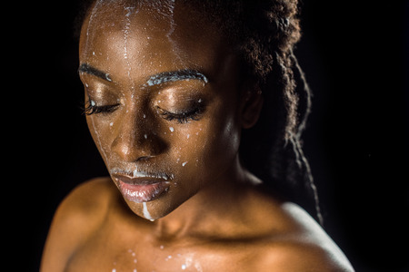 beautiful sensual young african american woman with spilled milk on face isolated on blackの写真素材