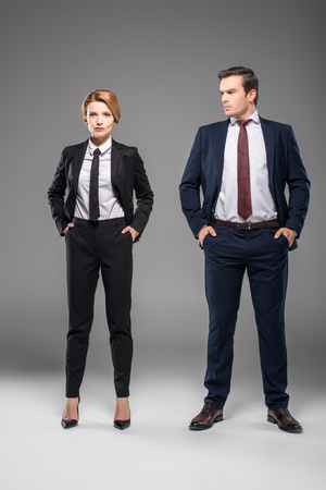 confident businesswoman and businessman standing with hands in pockets, isolated on greyの写真素材