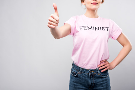 cropped view of woman in pink feminist t-shirt showing thumb up, isolated on greyの写真素材