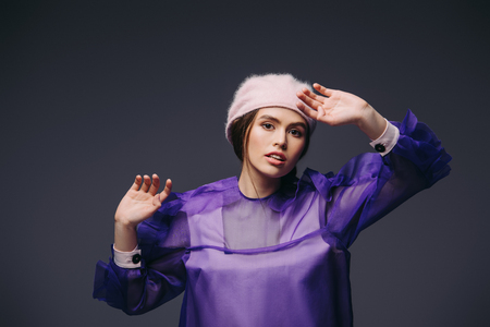 portrait of beautiful woman in fashionable purple dress and hat looking at camera on black backgroundの写真素材