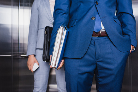 Cropped view of businessman with folders and woman with briefcase riding an elevatorの写真素材