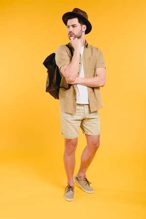 Full length view of young man in shorts with backpack looking away isolated on yellow backgroundの写真素材