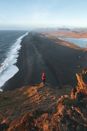 Back view of person standing on cliff and looking at majestic ocean, Vik Dyrholaey, Reynisfjara...