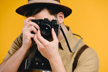 Young male photographer photographing with camera isolated on yellow backgroundの写真素材