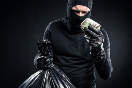 Man in balaclava holding plastic bag with cash and dollarsの写真素材
