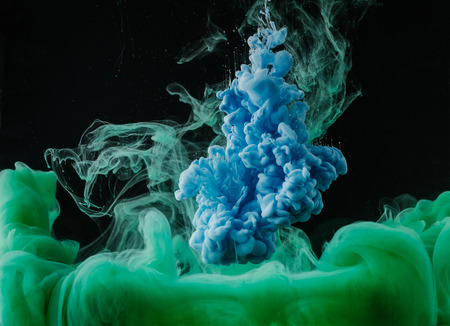 Close-up view of abstract green and blue flowing paint on black backgroundの写真素材