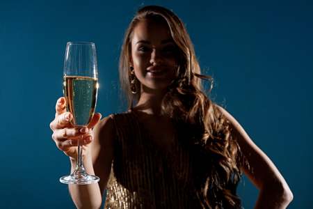 Attractive woman showing glass of champagne in evening isolated on blue backgroundの写真素材