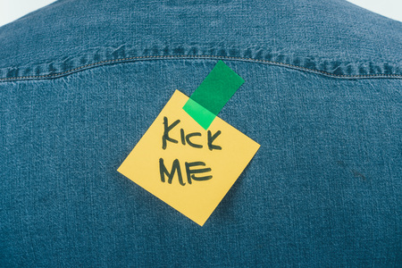 Close up view of note with kick me lettering on jeans shirt, April fools day concept