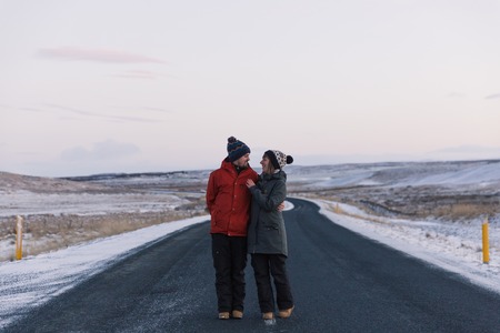 Happy young couple embracing and looking at each other while standing on asphalt road in Icelandの写真素材