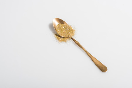 Golden spoon and bright sand on white backgroundの写真素材
