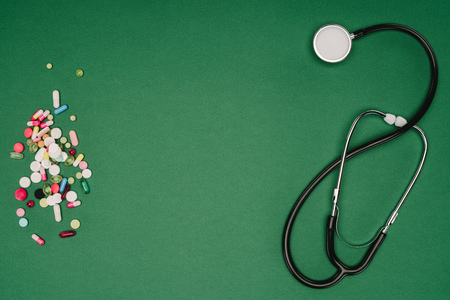 Flat lay with arranged pills and stethoscope isolated on green tabletop, world health day concept