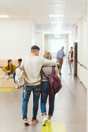 Rear view of teenage students couple walking by school corridor and embracingの写真素材