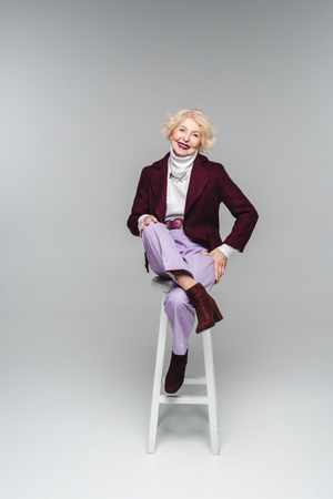 Happy senior woman in stylish clothes sitting on chair on grey backgroundの写真素材