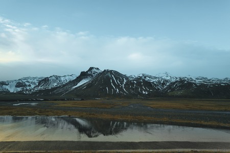 Beautiful rocky mountains with snow reflected in calm water of lagoon, Icelandの写真素材