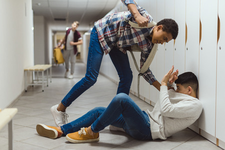 Frightened schoolboy being bullied by classmate in school corridor under lockers while other boy running to help himの写真素材