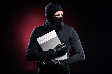Criminal in balaclava holding confidential documentsの写真素材