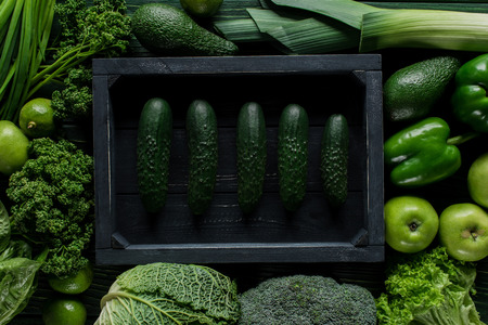 Top view of cucumbers in wooden box between green vegetables, healthy eating conceptの写真素材