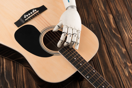 Cropped shot of robot touching strings of acoustic guitar over wooden surfaceの写真素材
