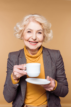 Happy fashionable senior woman with coffee cup isolated on beige backgroundの写真素材
