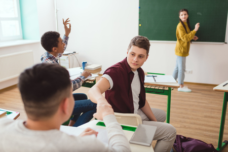 Multicultural high school students doing fist bump and classmates behind in classroomの写真素材