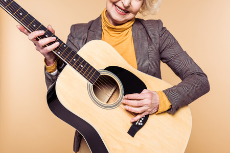 Cropped image of stylish woman playing on acoustic guitar isolated on beige backgroundの写真素材