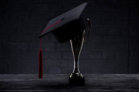 Graduation cap on trophy cup on wooden tableの写真素材