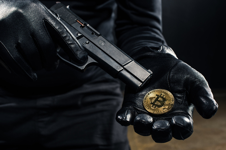 Close-up view of gun and bitcoin in hands of thiefの写真素材