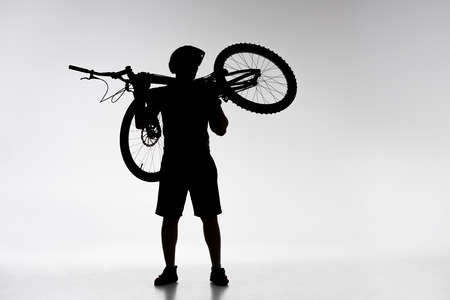 Silhouette of trial biker holding bicycle on shoulders on white backgroundの写真素材