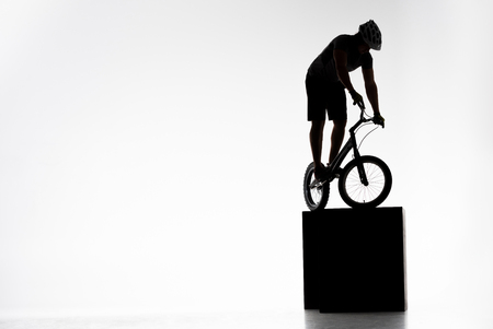 Silhouette of trial cyclist balancing on obstacles on white backgroundの写真素材