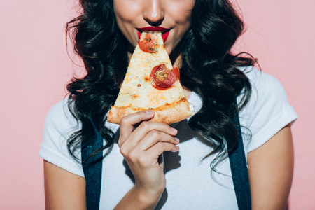 Cropped shot of woman eating pizza on pink backgroundの写真素材