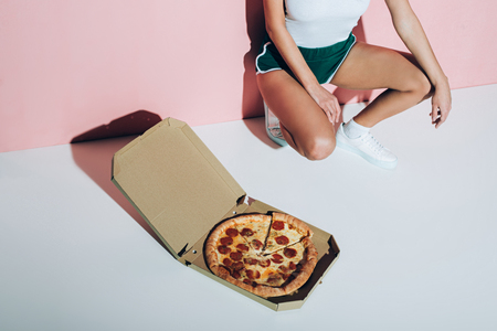 Partial view of stylish woman and delivery box with pizza on floor on pink backdropの写真素材