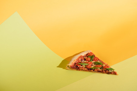 Close up view of piece of pizza with cherry tomatoes and basil on colorful backdropの写真素材