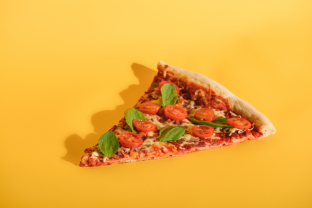 Close up view of piece of pizza with cherry tomatoes and basil on orange backdropの写真素材