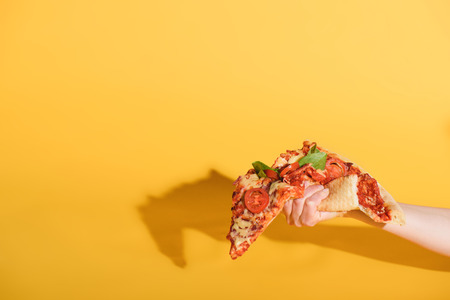 Partial view of woman squeezing piece of pizza in hand on yellow backgroundの写真素材