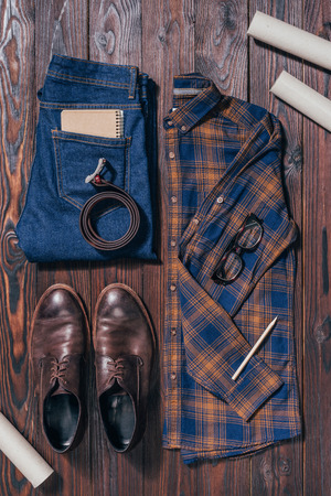 Flat lay with male shirt, shoes, jeans, eyeglasses and architectural blueprints arranged on wooden surfaceの写真素材
