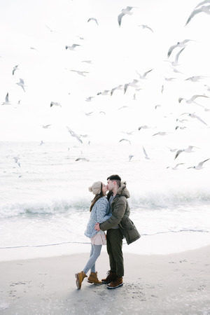 Couple hugging and kissing on winter sea shore with seagulls