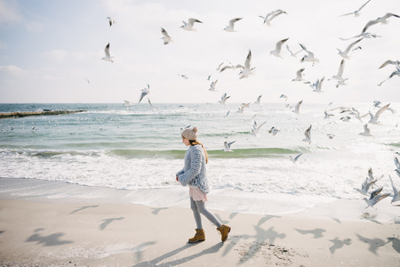 Beautiful stylish girl on winter seashore with seagullsの写真素材