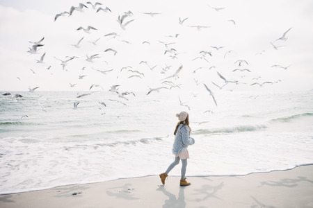 Stylish girl running on winter seashore with seagullsの写真素材