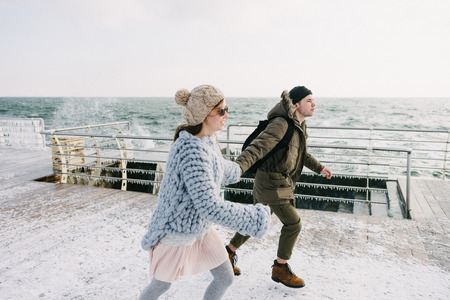 Young couple holding hands and running on winter quayの写真素材