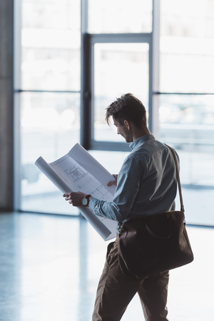 Side view of architect looking at blueprint in hands in empty buildingの写真素材