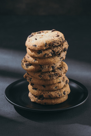 Stack of delicious chocolate-chip cookies on black plate