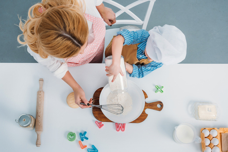 Top view of mother and boy pouring milk into bowl with egg and flourの写真素材
