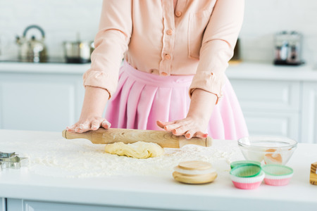 Cropped image of woman rolling dough with rolling pin at kitchen