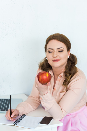Beautiful woman looking at apple in kitchenの写真素材