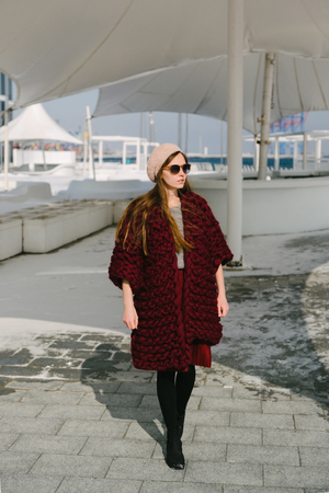 Stylish young woman in burgundy merino wool cardigan walking on quayの写真素材
