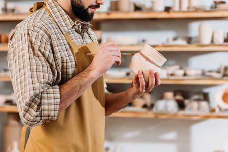 Cropped view of male potter painting ceramic dishware with brush in workshopの写真素材