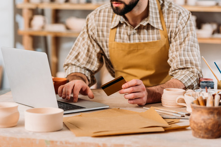 Cropped view of potter shopping online with laptop and credit card in workshopの写真素材