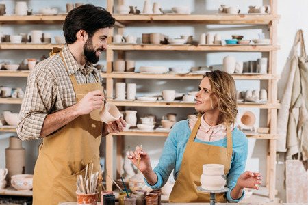 Smiling potters painting ceramic dishware in workshopの写真素材
